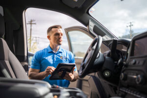 Planet Roof team member using a tablet beside a work vehicle during a roofing appointment.
