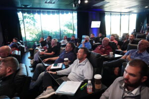Group of focused business founders and home service operators sitting in rows taking notes with laptops during a private corporate strategy session at the Build It To Sell It Mastermind conference.