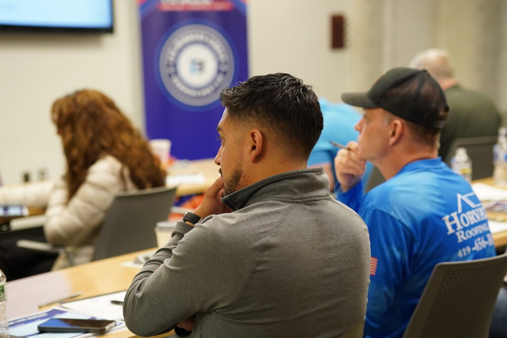 Side profile of a focused roofing contractor wearing a Horvath Roofing long-sleeve shirt sitting at a seminar table analyzing a corporate business growth presentation.