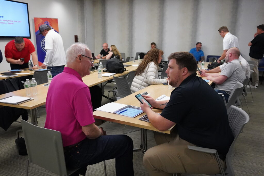 Diverse group of business owners and home service contractors collaborating in workshop breakout groups at tables during a Build It To Sell It Winners Circle strategy seminar.