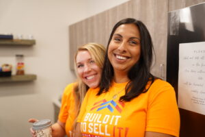 Danielle and Alicia smiling together in Build It to Sell It orange branded t-shirts at the Mastermind event.
