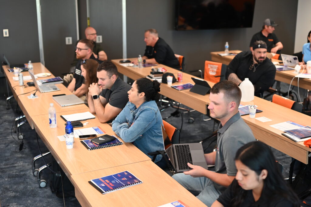 Home service business owners seated at conference tables with laptops and workbooks, engaged in a Build It to Sell It Mastermind event session.