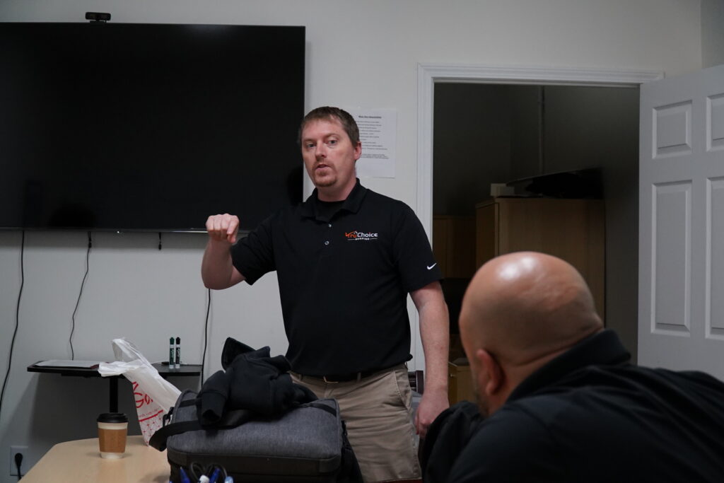 A Tru Choice Roofing manager leading an internal team meeting and training workshop in front of a conference room monitor display screen.